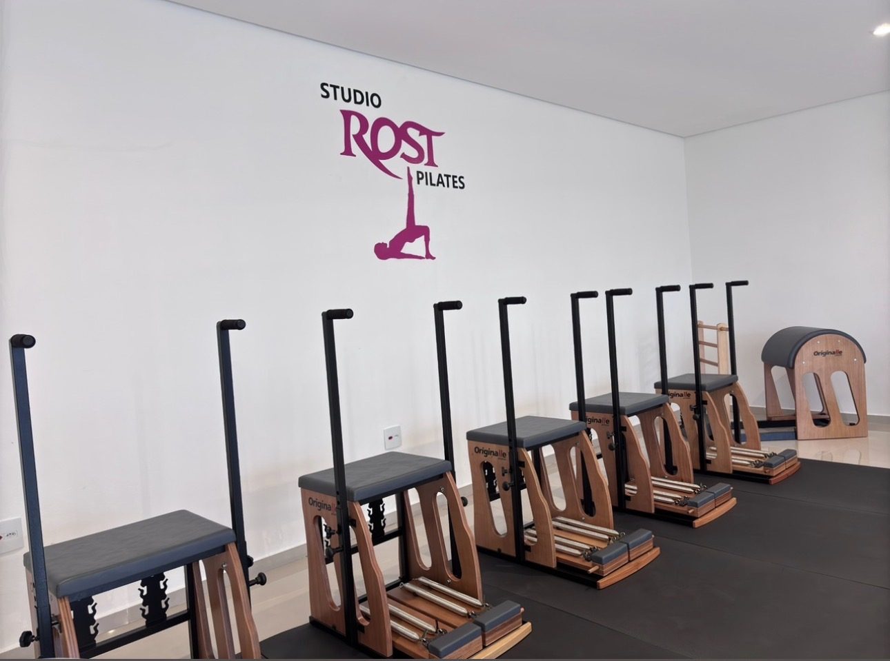 Chairs e Barrel de pilates alinhados na parede com o logo do Rost